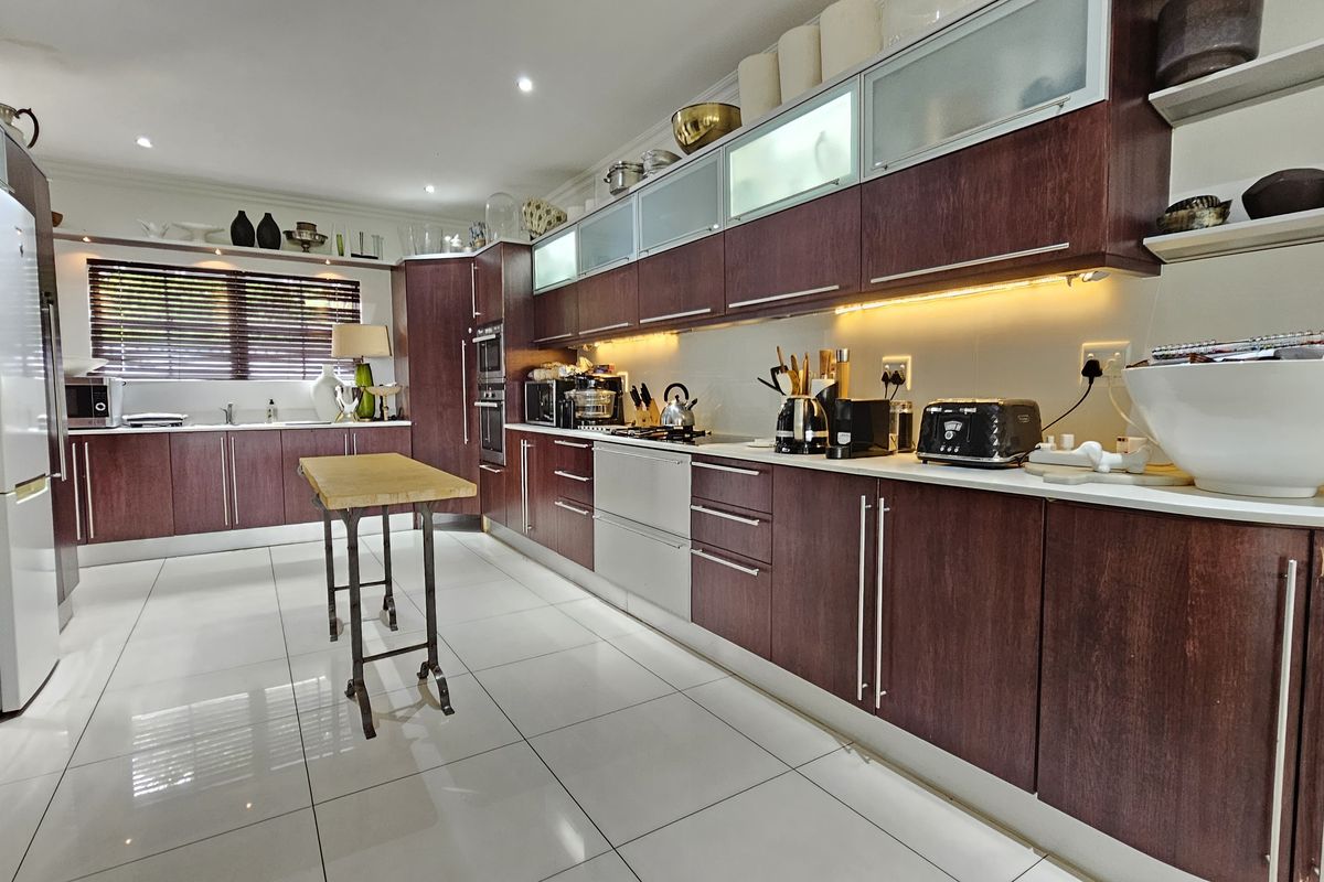 A spacious, well-lit kitchen featuring dark wood cabinetry, modern tiled flooring, integrated appliances, and ample counter space for meal preparation.
