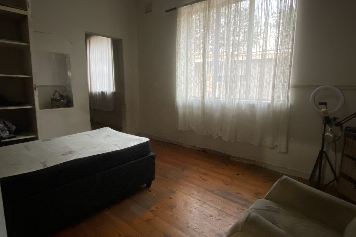 A bedroom featuring original hardwood flooring, built-in shelving, and a recessed wall niche, requiring cosmetic updates to the walls and finishes.