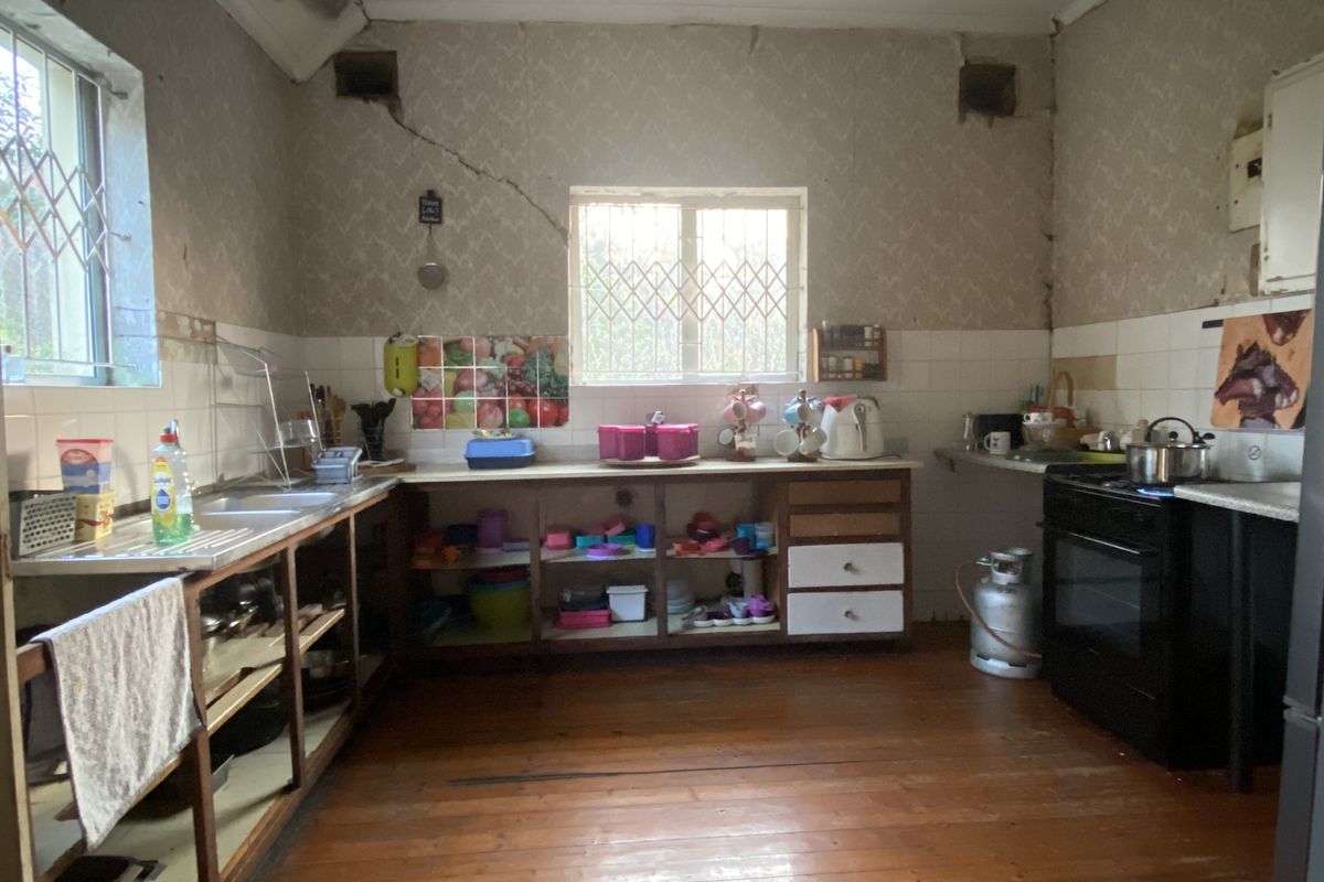 A dated kitchen featuring timber flooring, built-in cabinetry, and a tiled splashback, currently requiring significant renovation and repair to the walls and ceiling.