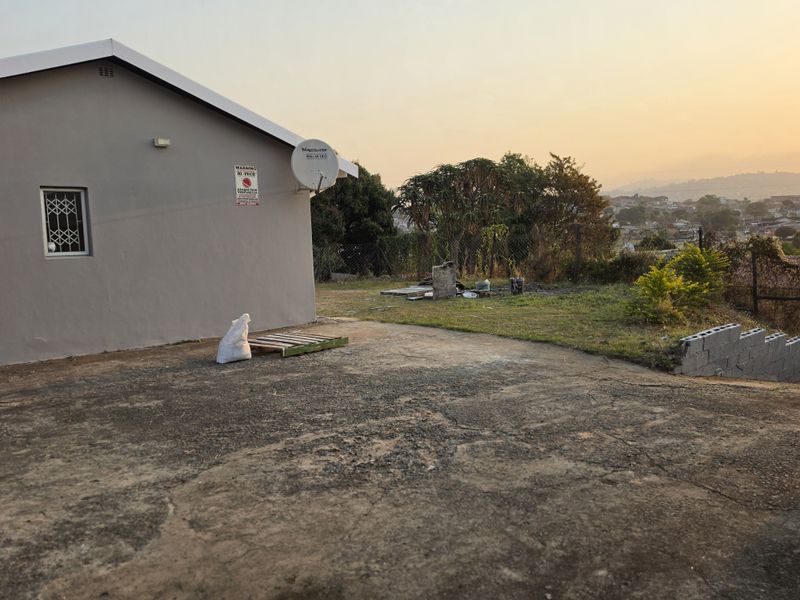 Rear exterior view of the property featuring a concrete driveway, security gate, and satellite dish with a view of the surrounding area.