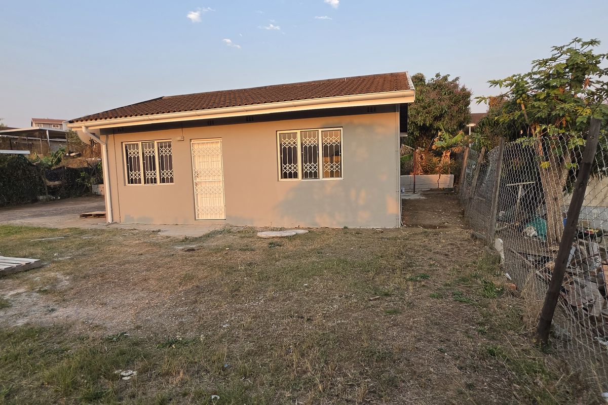 Rear view of a single-story house featuring a tiled roof, security bars on windows, and a security gate, set on a large unlandscaped plot.