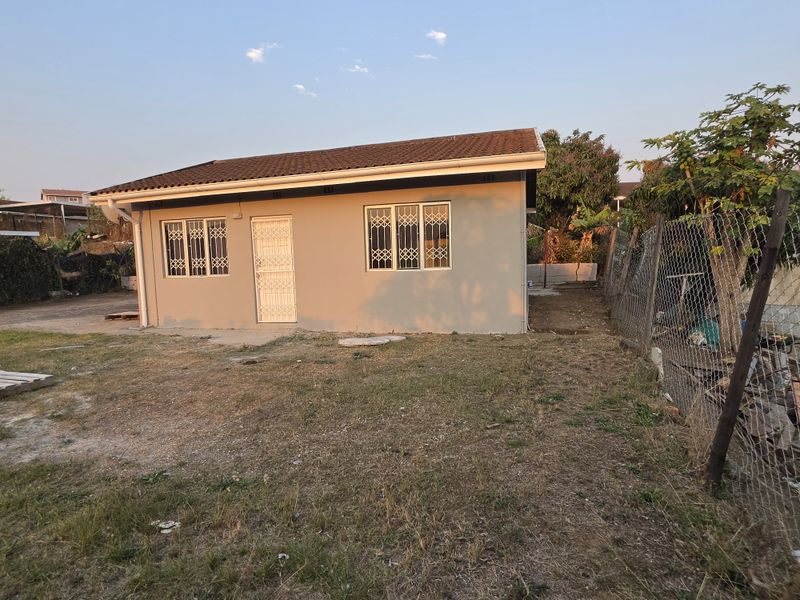 Rear view of a single-story house featuring a tiled roof, security bars on windows, and a security gate, set on a large unlandscaped plot.