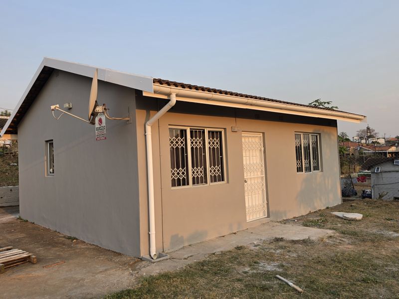 A well-maintained single-story residential house featuring a neutral grey exterior, secure window bars, and a tiled roof.