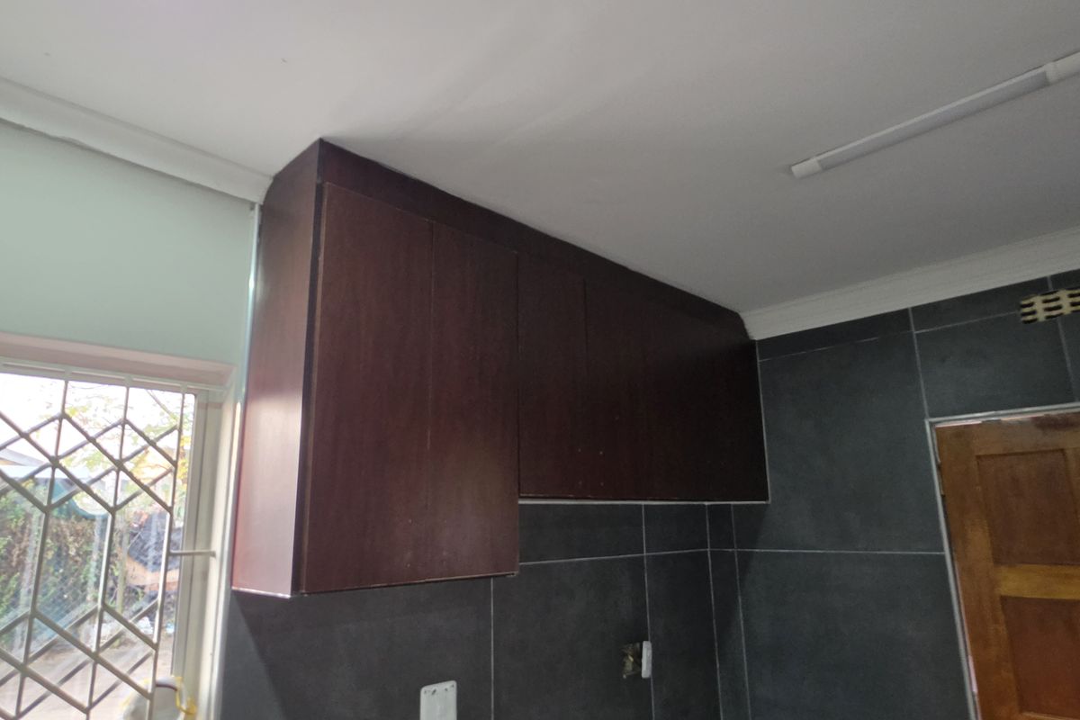 A kitchen area featuring dark wood cabinetry and dark grey wall tiles, providing a neutral base for potential modern updates.