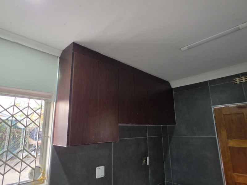 A kitchen area featuring dark wood cabinetry and dark grey wall tiles, providing a neutral base for potential modern updates.