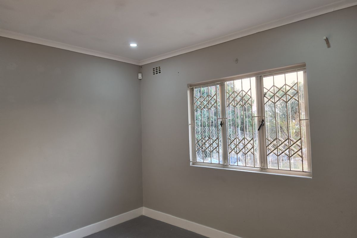 A clean, empty bedroom featuring neutral grey walls, recessed downlighting, and security bars on the window.
