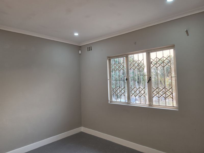 A clean, empty bedroom featuring neutral grey walls, recessed downlighting, and security bars on the window.