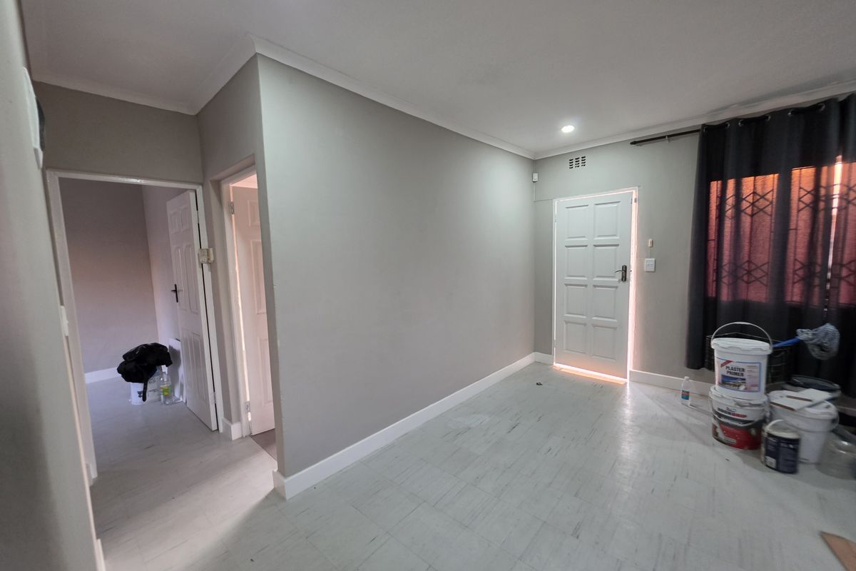 An empty living area featuring neutral grey walls, tiled flooring, recessed lighting, and access to adjacent rooms via internal doors.