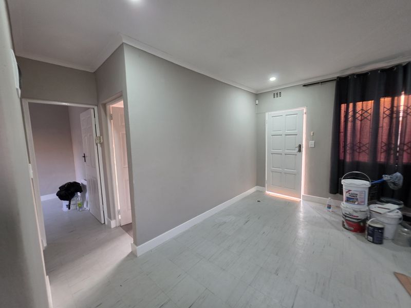 An empty living area featuring neutral grey walls, tiled flooring, recessed lighting, and access to adjacent rooms via internal doors.