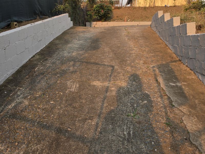 A sloped concrete driveway flanked by painted masonry retaining walls and secured with perimeter razor wire fencing.