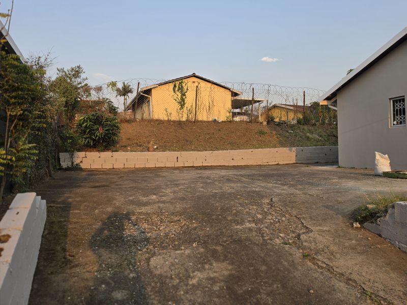 Rear exterior area featuring a concrete driveway, retaining wall, and perimeter security fencing with razor wire.