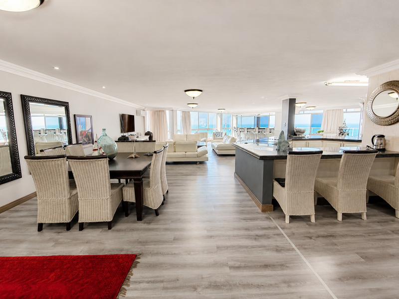 Spacious open-plan living and dining area featuring a modern kitchen island, light laminate flooring, and expansive windows with ocean views.