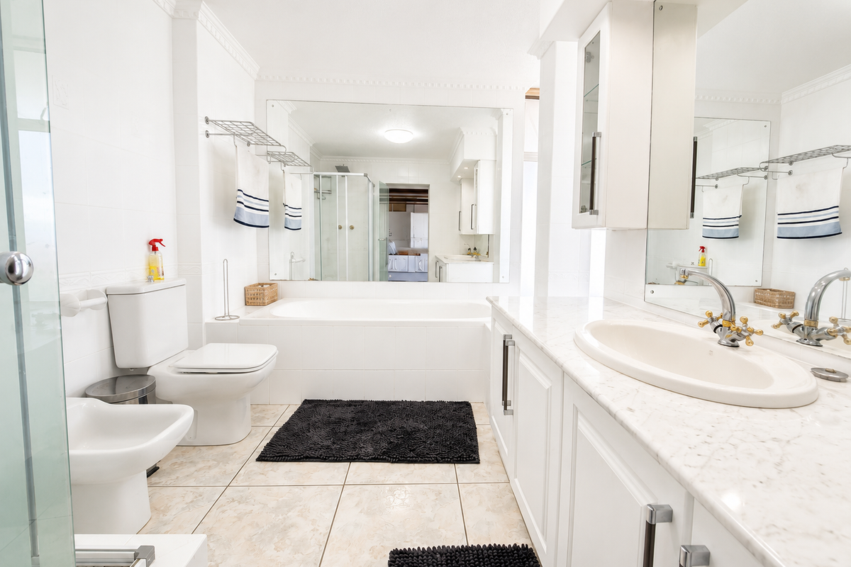 A bright, well-maintained bathroom featuring a marble-topped vanity, built-in bathtub, bidet, toilet, and a spacious glass-enclosed shower area.