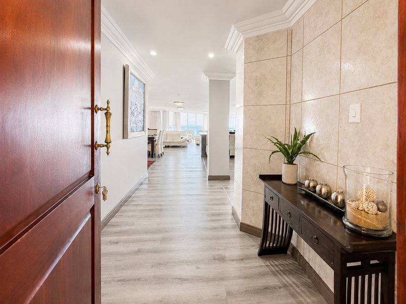 Welcoming apartment entrance featuring light-toned laminate flooring, decorative tiled wall accents, and recessed lighting, leading into an open-plan living area.