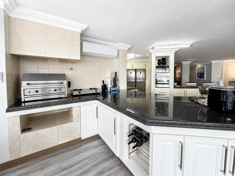 Spacious kitchen featuring granite countertops, built-in braai, gas hob, integrated oven and microwave, and ample cabinetry with a dedicated wine storage rack.