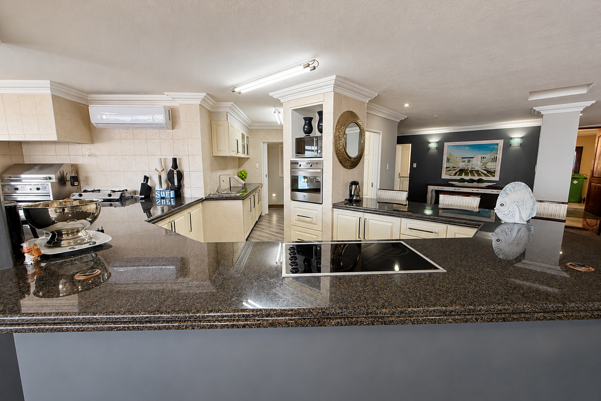 Spacious kitchen featuring granite countertops, built-in oven and microwave, electric hob, and ample cabinetry, seamlessly integrated into an open-plan living area.