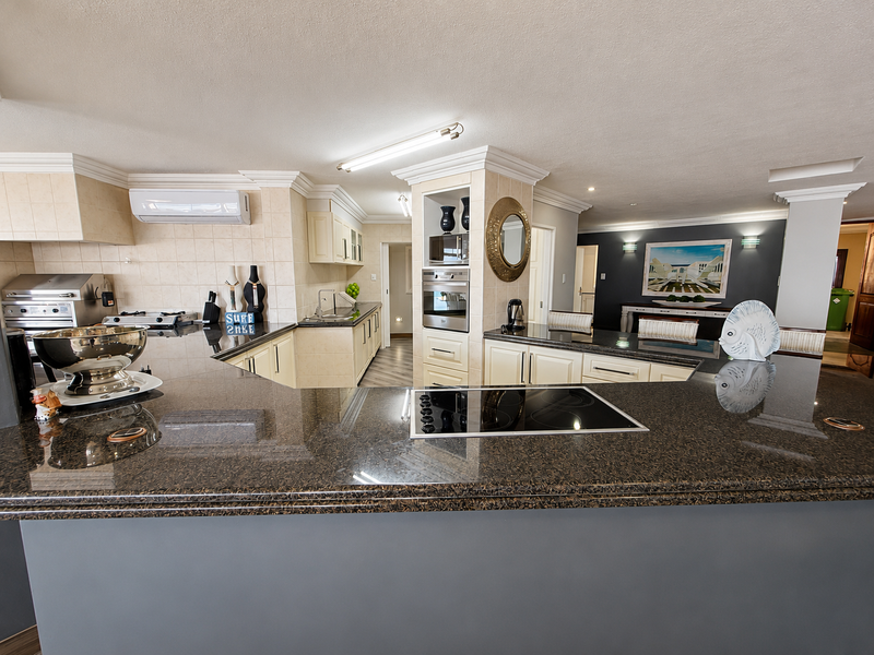 Spacious kitchen featuring granite countertops, built-in oven and microwave, electric hob, and ample cabinetry, seamlessly integrated into an open-plan living area.