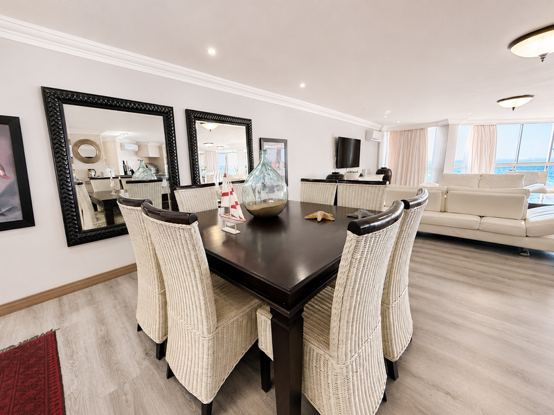 Spacious open-plan living and dining area featuring modern laminate flooring, recessed lighting, crown molding, and large sliding doors with ocean views.