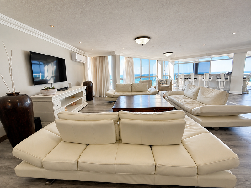 Spacious open-plan living area featuring modern flooring, recessed lighting, and a breakfast bar, with expansive windows offering panoramic ocean views.