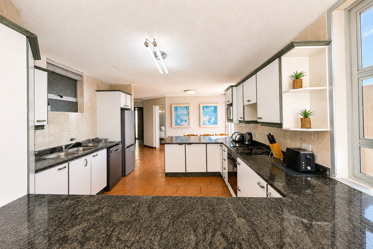 A functional kitchen featuring granite countertops, ample built-in cabinetry, a double basin sink, and integrated cooking appliances with tiled flooring.