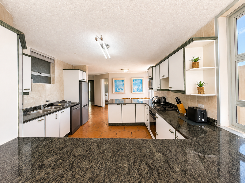 A functional kitchen featuring granite countertops, ample built-in cabinetry, a double basin sink, and integrated cooking appliances with tiled flooring.