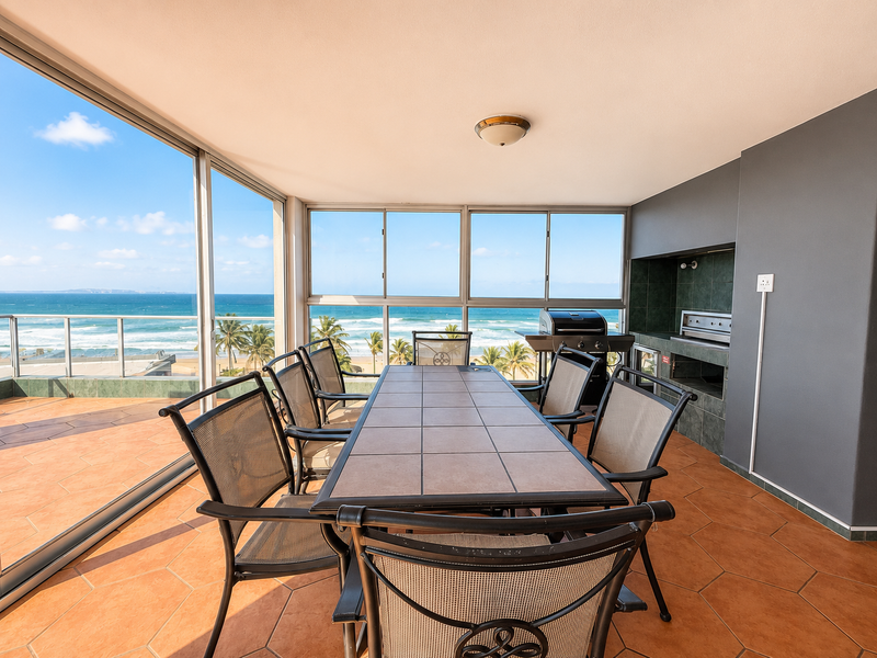 Enclosed balcony featuring tiled flooring, a built-in braai, and expansive sliding glass doors offering panoramic ocean views.