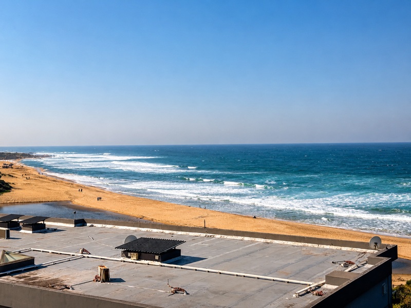 A scenic elevated view overlooking the coastline, sandy beach, and ocean, captured from the rooftop of the apartment building.