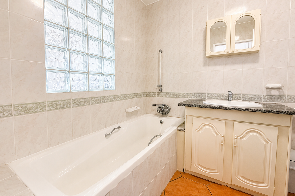 A functional bathroom featuring a bathtub, vanity cabinet with granite countertop, and a distinctive glass block window, finished with neutral wall tiles.