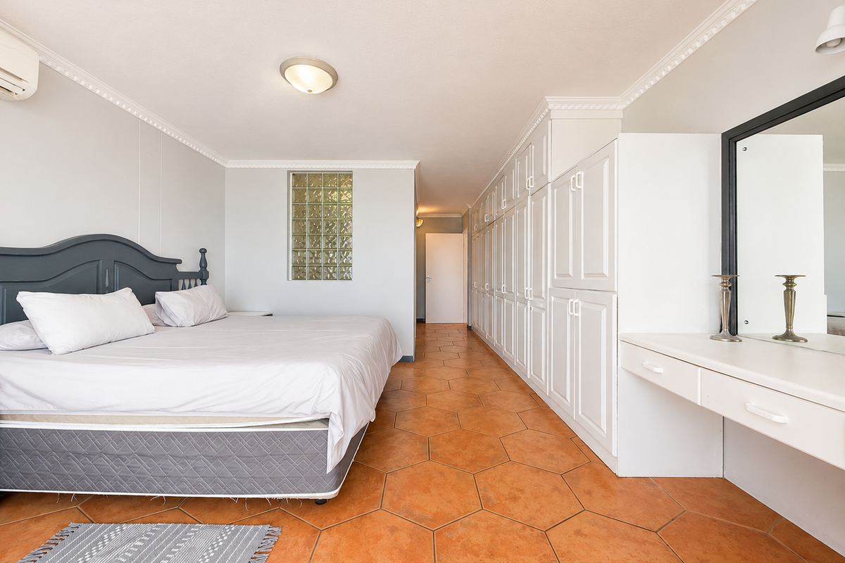 Spacious bedroom featuring extensive built-in cabinetry, a vanity unit, terracotta flooring, and a unique glass block feature window.