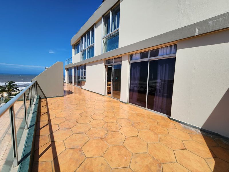 Spacious balcony featuring a glass balustrade, hexagonal tiled flooring, and direct access to the apartment through large sliding glass doors with ocean views.