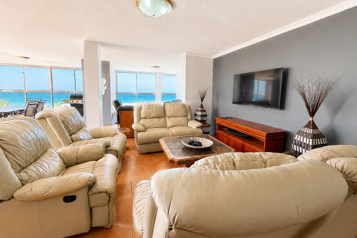 Spacious living room featuring terracotta floor tiles, an accent wall, and large sliding glass windows offering expansive ocean views.