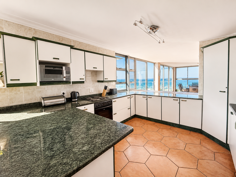 A functional kitchen featuring built-in appliances, ample cabinetry, and tiled flooring, with large windows offering expansive ocean views.