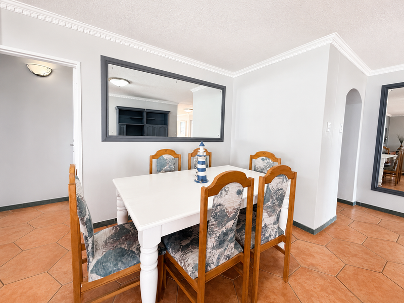 A bright dining area featuring terracotta floor tiles, decorative crown molding, and a large wall-mounted mirror, creating an open and connected living space.