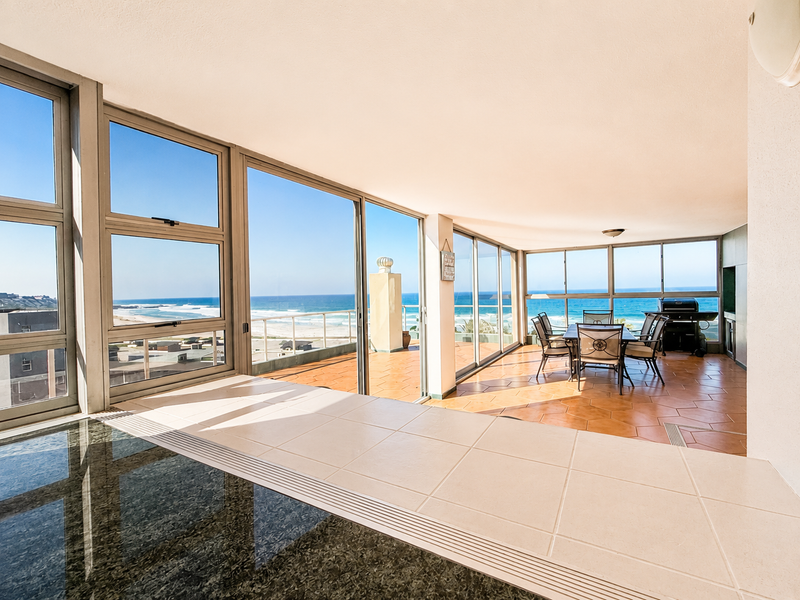 Spacious enclosed balcony featuring large sliding glass doors, tiled flooring, and panoramic ocean views, perfect for indoor-outdoor entertaining.