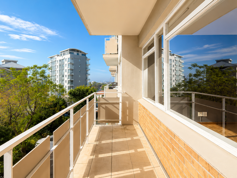 A spacious, well-maintained balcony featuring tiled flooring, a metal balustrade, and large windows offering an elevated urban view.