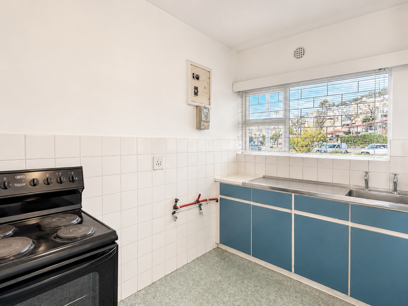 A functional kitchen featuring a freestanding electric stove, stainless steel sink, tiled splashback, and blue cabinetry with ample counter space.