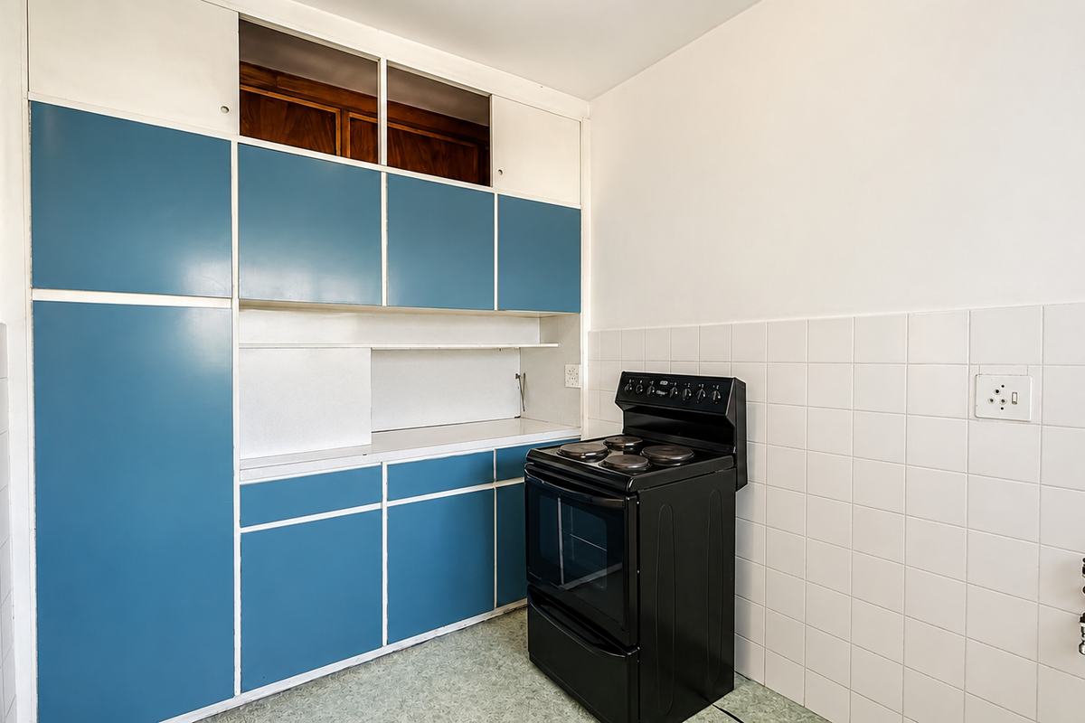 A functional kitchen area featuring blue built-in cabinetry, a black electric stove, and white tiled splashbacks, ready for modernization.