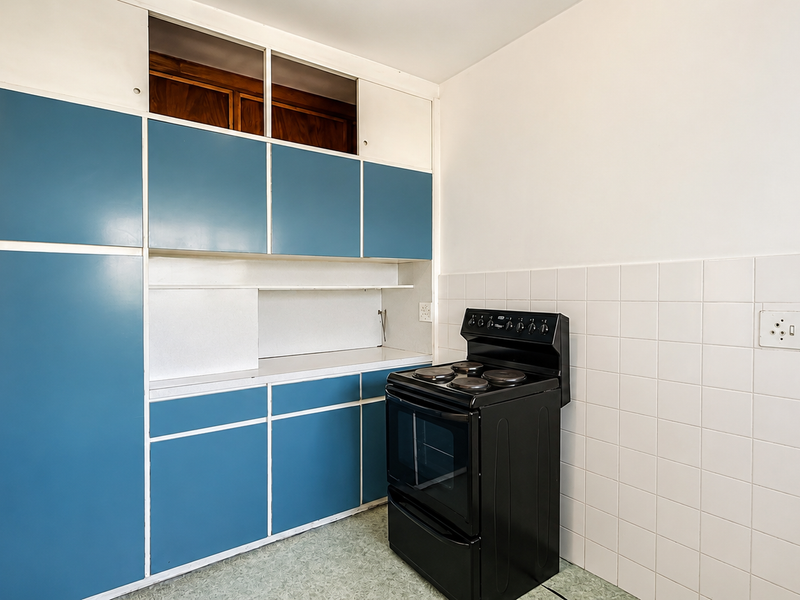 A functional kitchen area featuring blue built-in cabinetry, a black electric stove, and white tiled splashbacks, ready for modernization.