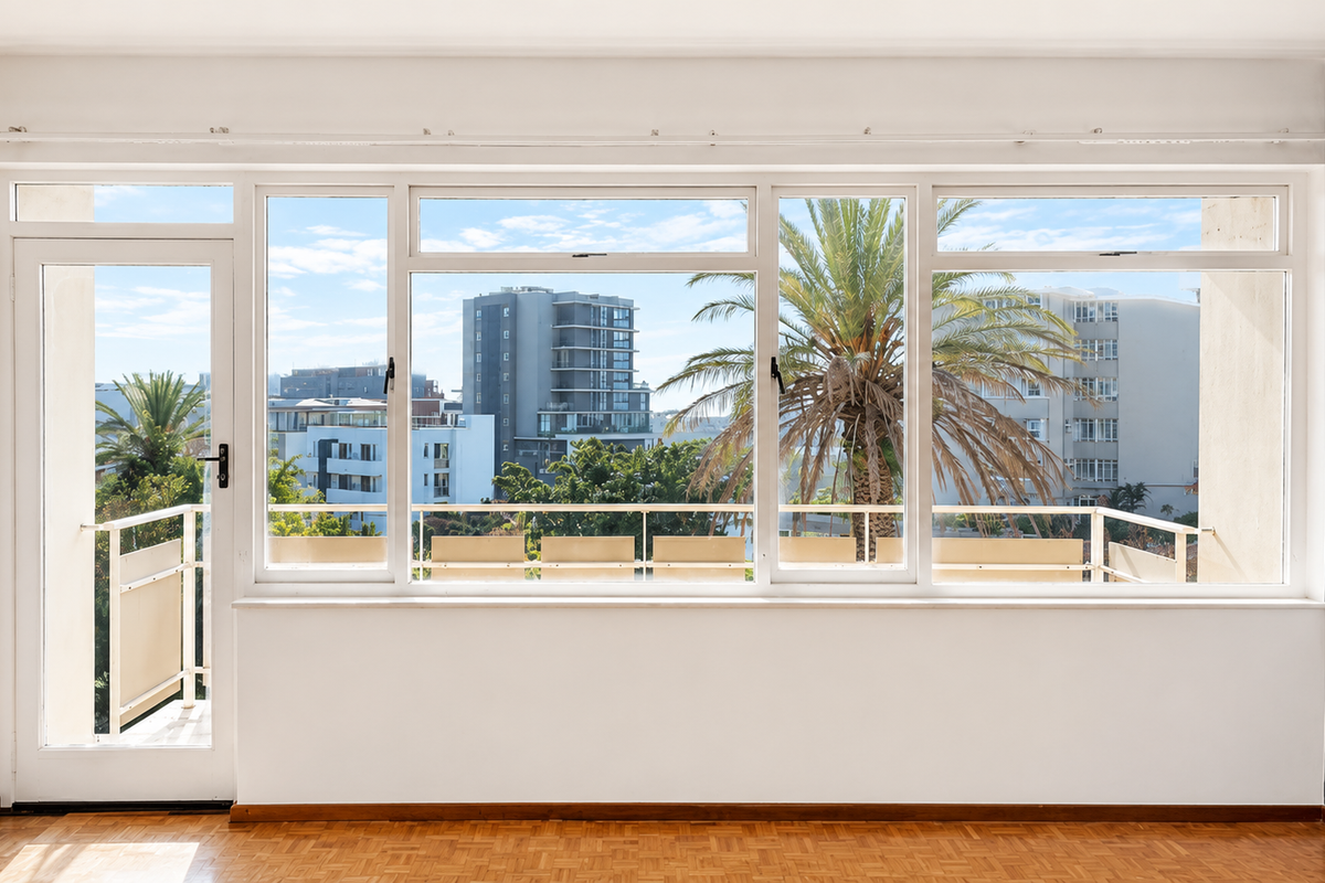 A bright, empty living room featuring classic parquet flooring, large windows, and direct access to a balcony with urban views.