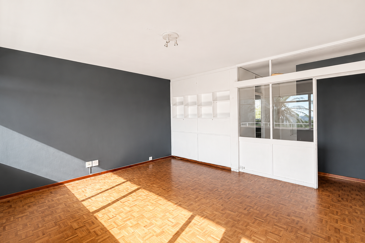 A bright, empty bedroom featuring classic parquet flooring, built-in storage shelving, and a modern glass partition wall allowing for natural light flow.