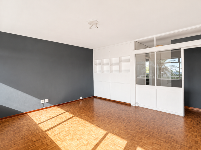 A bright, empty bedroom featuring classic parquet flooring, built-in storage shelving, and a modern glass partition wall allowing for natural light flow.