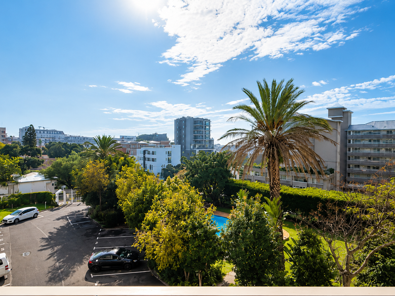 Elevated view overlooking the apartment complex grounds, featuring a swimming pool, landscaped gardens, and dedicated parking area.