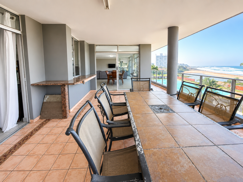 Spacious covered balcony featuring a built-in bar counter, tiled flooring, and a glass balustrade with panoramic ocean and pool views.