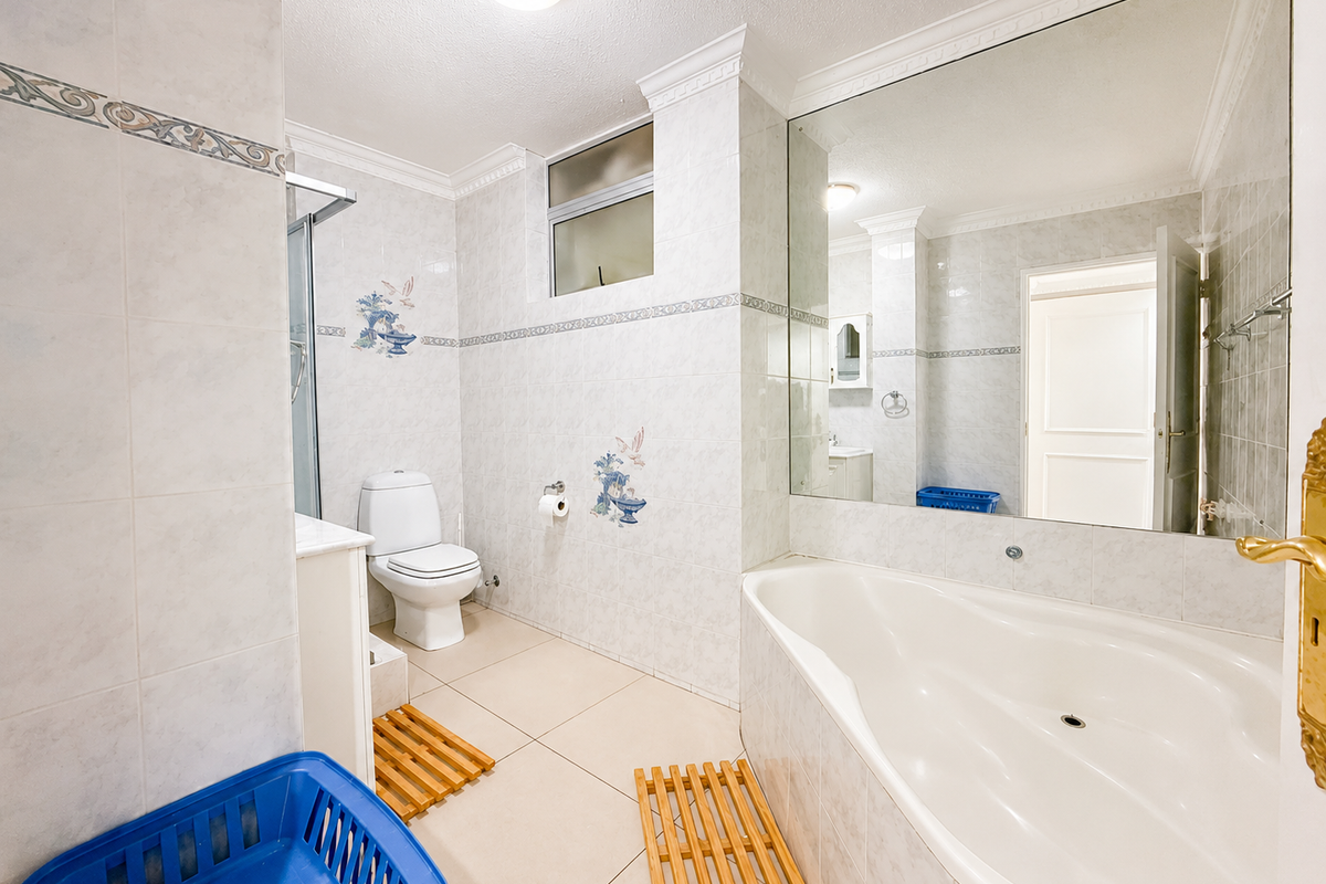 A functional bathroom featuring a built-in bathtub, separate shower enclosure, toilet, and a large wall-mounted mirror with classic tiled finishes.