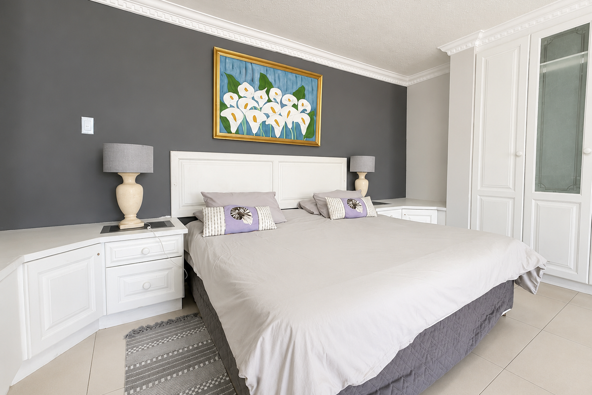 A well-maintained bedroom featuring built-in white cabinetry, bedside tables, crown molding, and neutral tiled flooring against a dark accent wall.