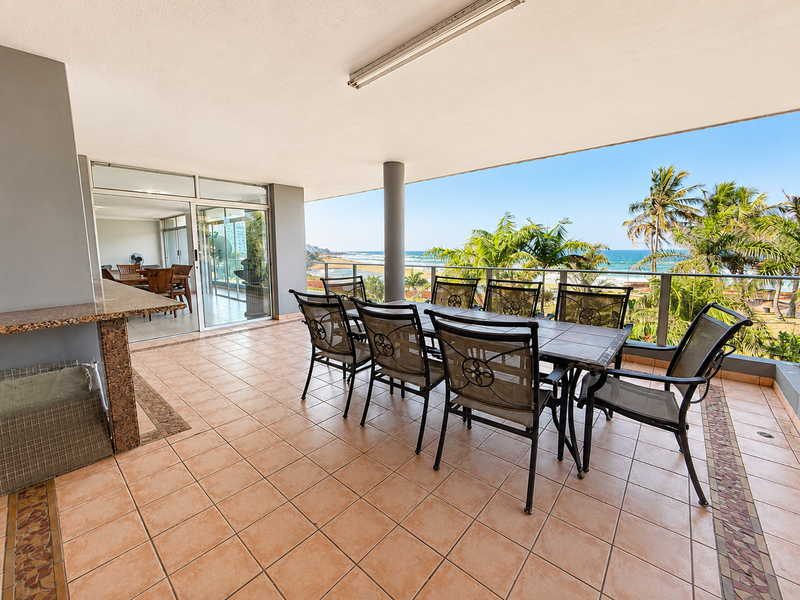 Spacious covered balcony featuring tiled flooring, a built-in granite serving counter, and a glass balustrade offering panoramic ocean views.
