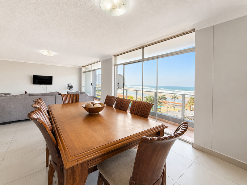 Spacious open-plan living and dining area featuring large sliding glass doors that open to a balcony with panoramic ocean views.