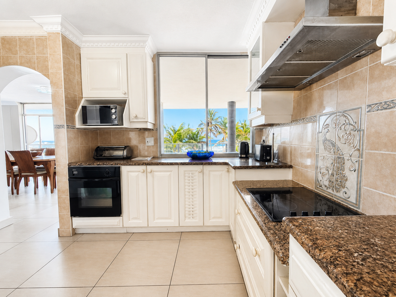 A well-maintained kitchen featuring granite countertops, built-in appliances, tiled splashbacks, and crown molding, with a view through the window to the exterior.