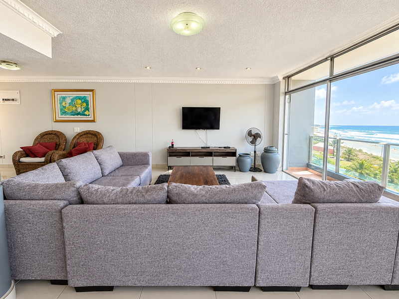 Spacious living room featuring tiled floors, crown molding, and large sliding glass doors opening to a balcony with ocean views.