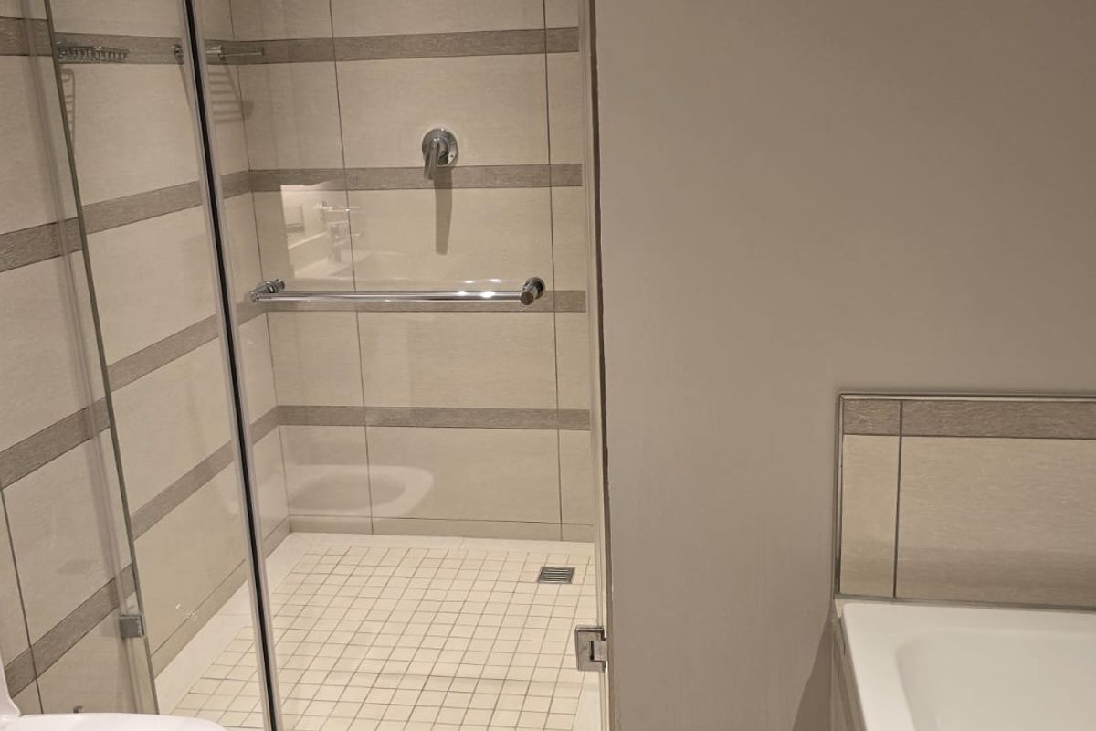 Modern bathroom featuring a glass-enclosed shower, built-in bathtub, and neutral ceramic wall tiling with a wall-mounted toilet flush system.